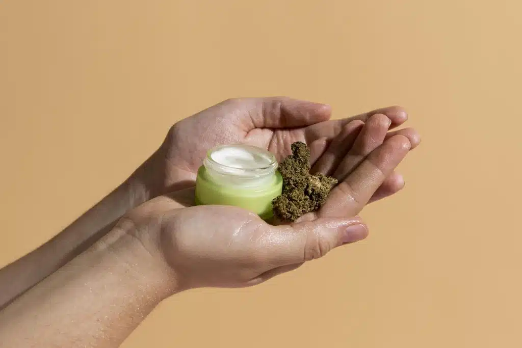 mani che reggono crema al cbd e piccole infiorescenze di cannabis